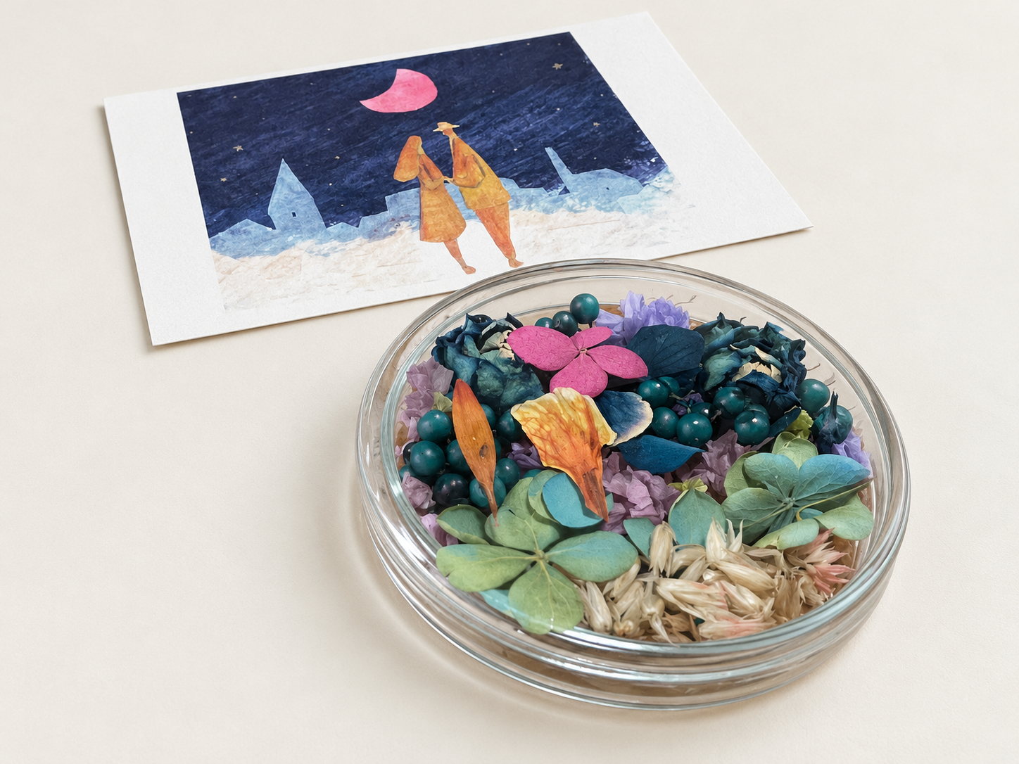ピンクの月と二人の人物が描かれた絵画と、青緑の花材を組み合わせたシャーレ作品
